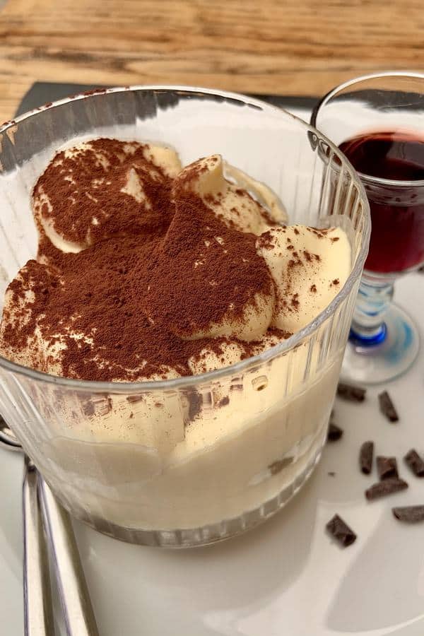 Tiramisu in a glass with a small cup of red wine on the side.