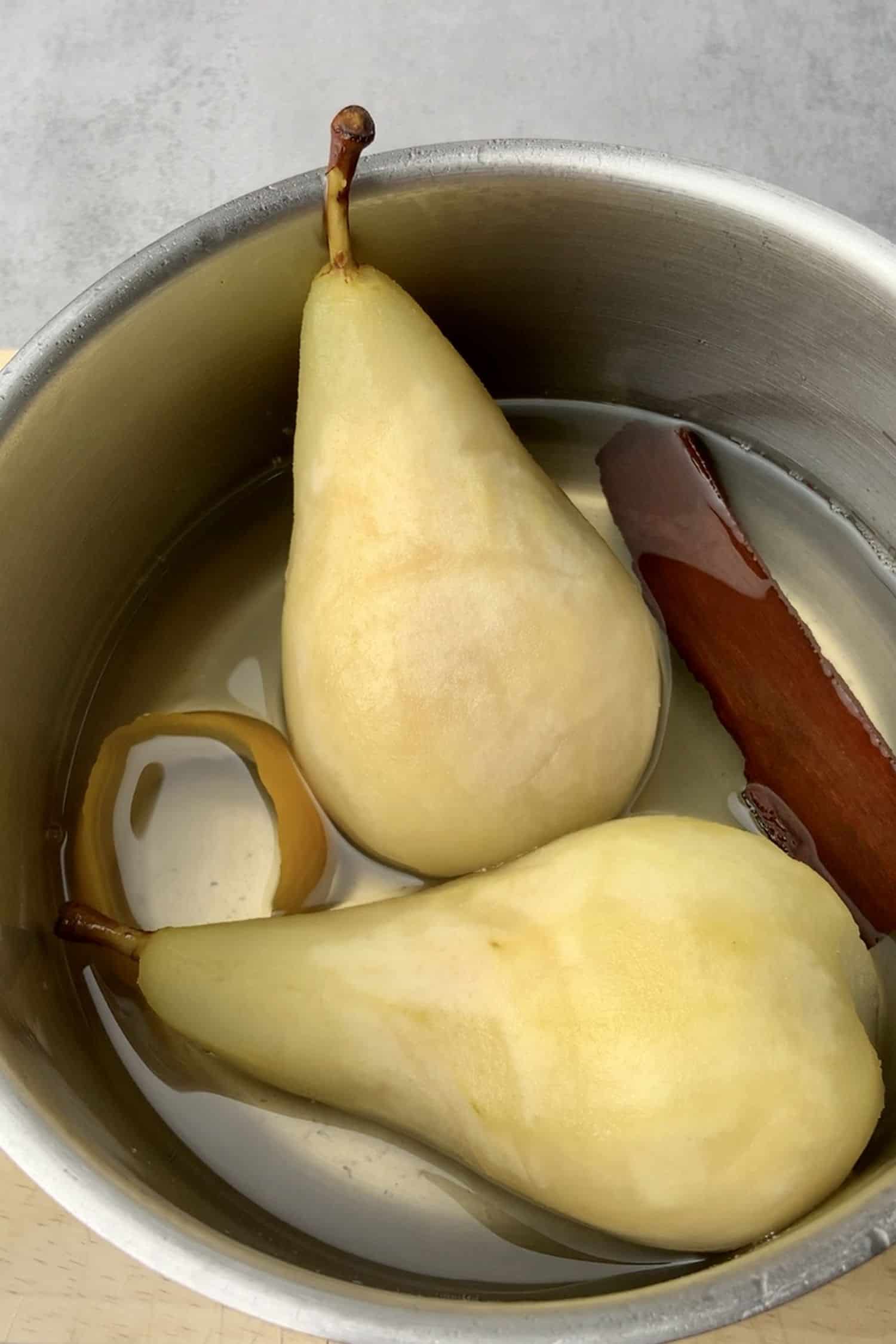 2 pears without skin in a pot with cinnamon sticks.