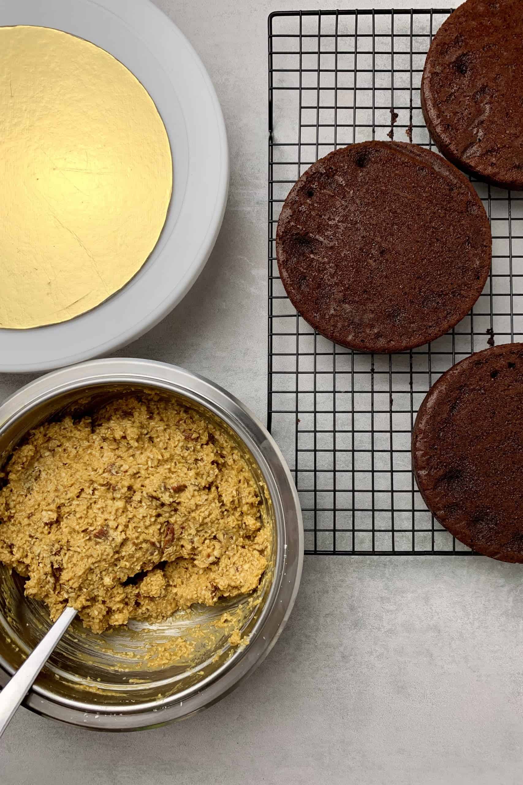 3 pcs of chocolate sponge on a cooling rack and the Butterscotch coconut pecan frosting in a bowl,