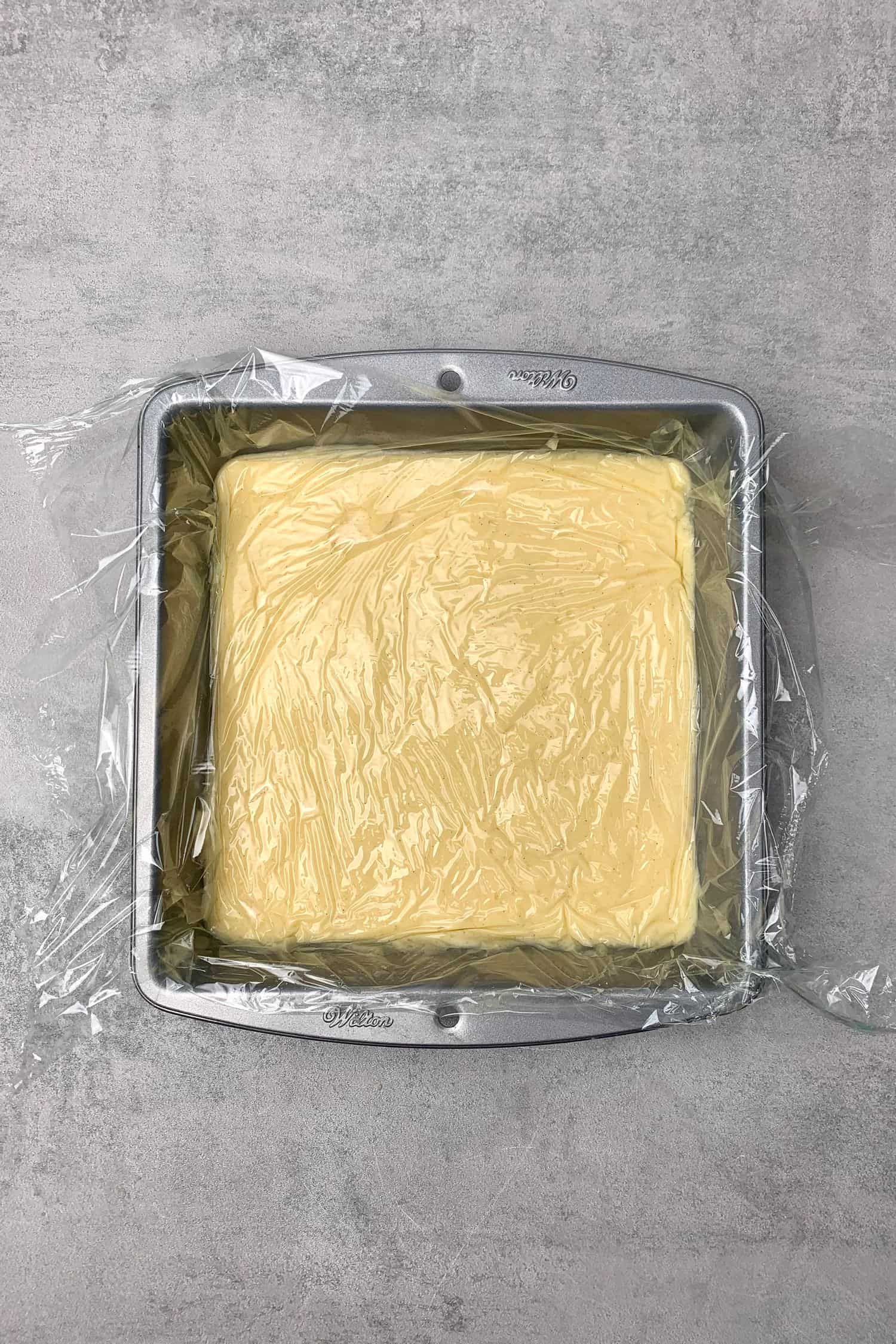 Pastry cream in a baking tin covered with plastic foil.