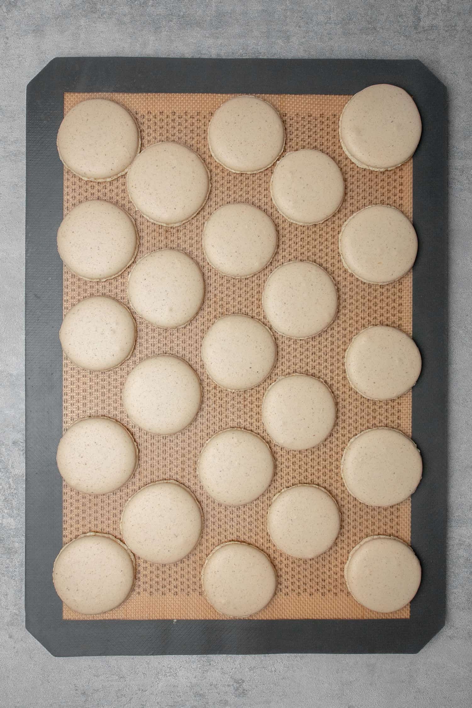 Chocolate hazelnut macaron shells on a baking mat.
