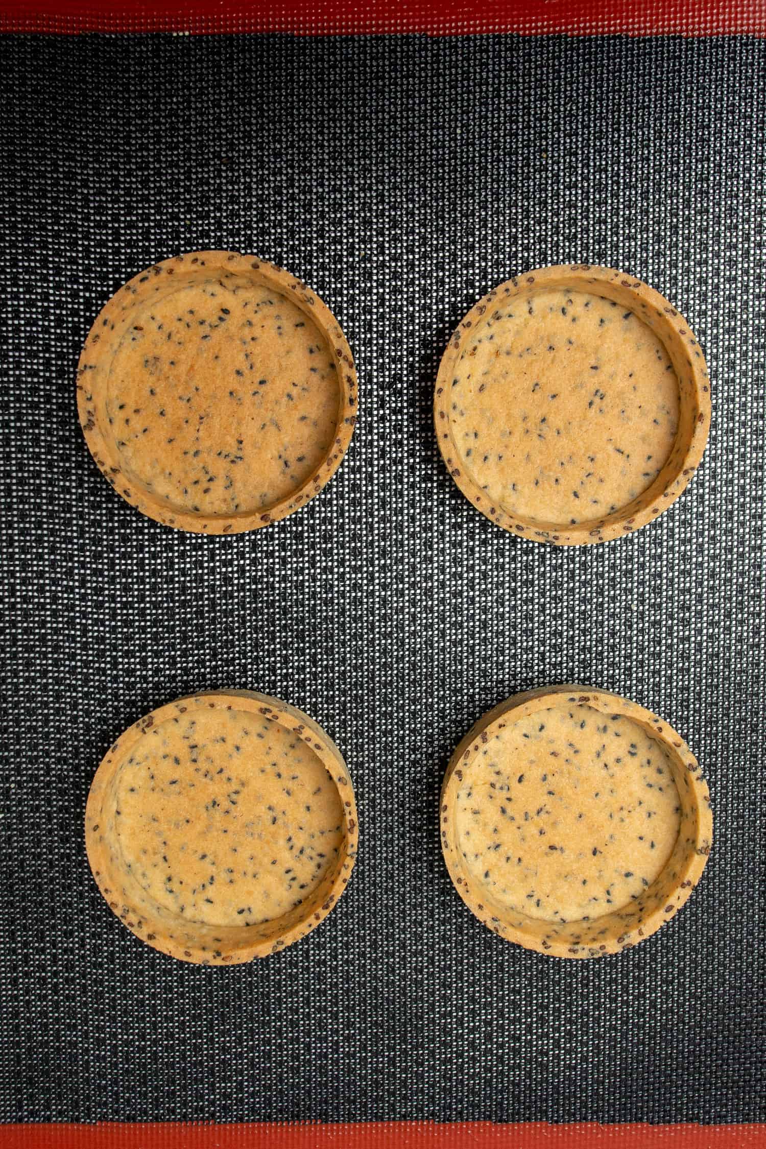 4 pcs of Black sesame Tart shells on a perforated baking mat.