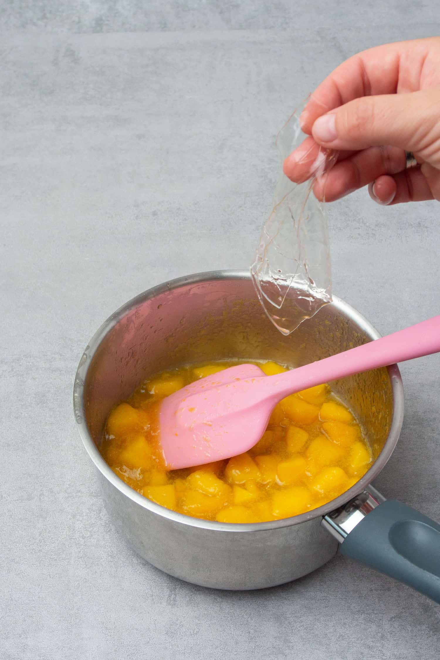 Adding gelatin to a pot of peach puree.