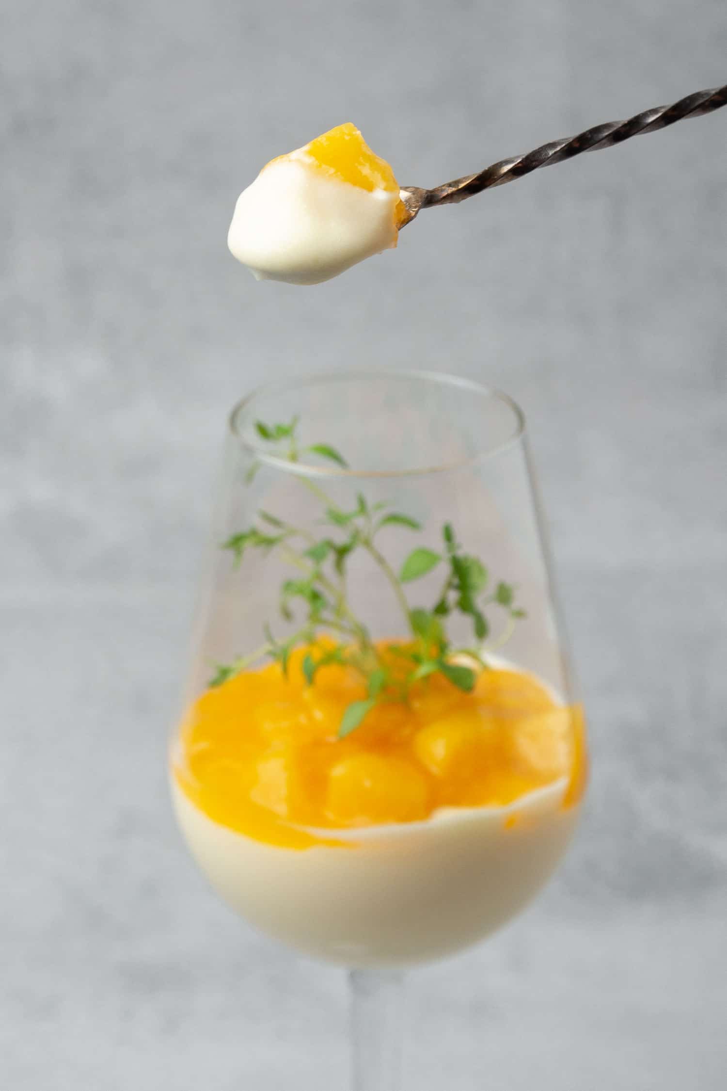 a scoop of Wine mousse Parfait with peach on a spoon with a glass in the background.