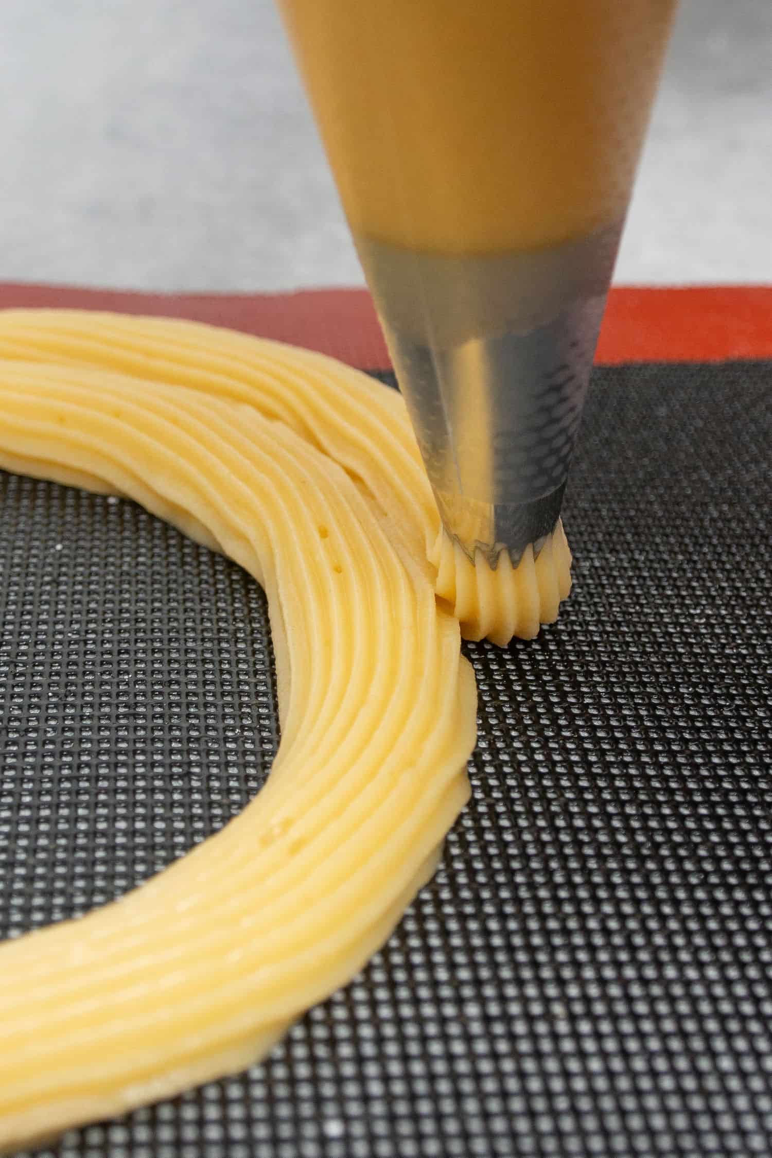 Piping the choux dough on a perforated  baking mat.