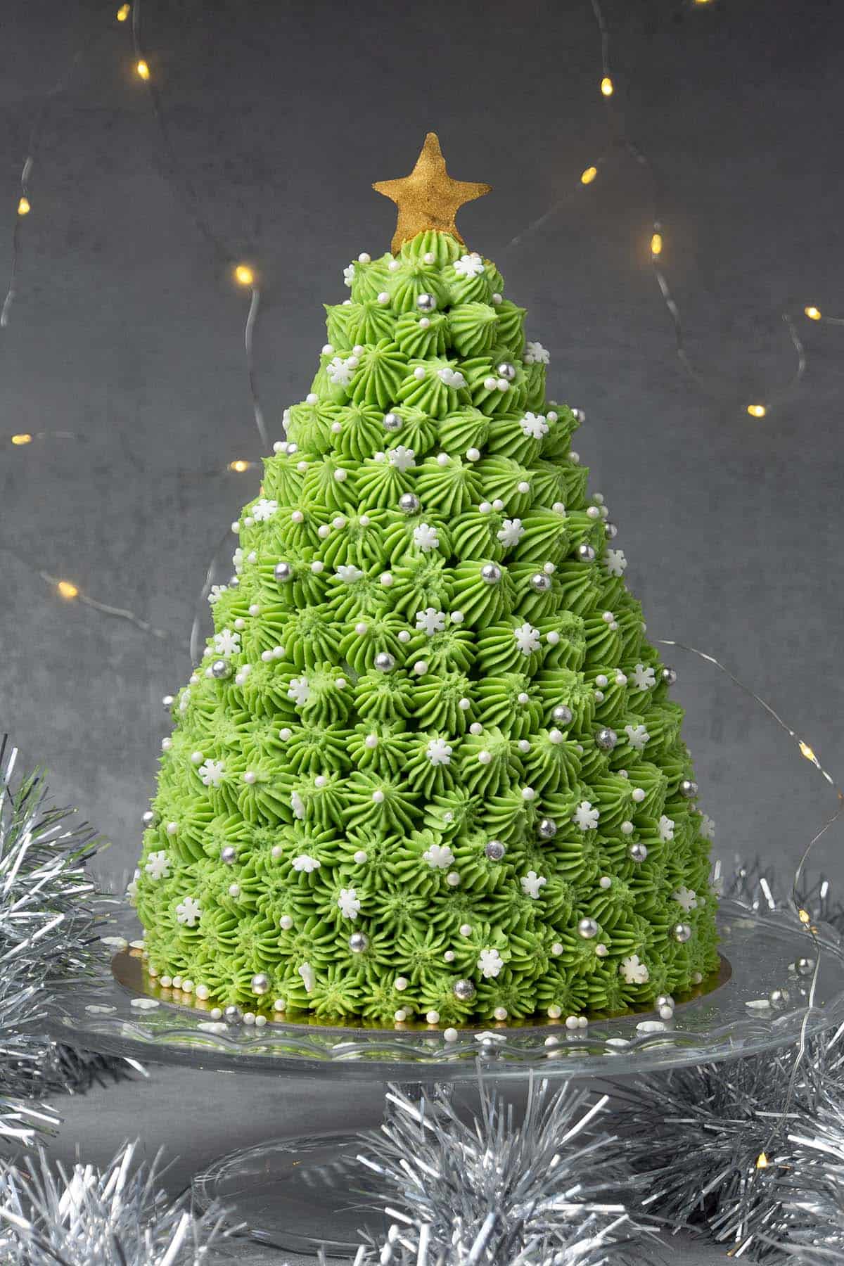 Christmas tree cake on a cake stand with lights in the background