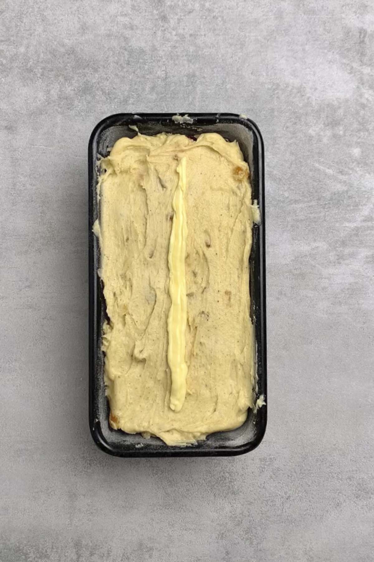 Bread mix in a loaf pan with a thin line of butter on top