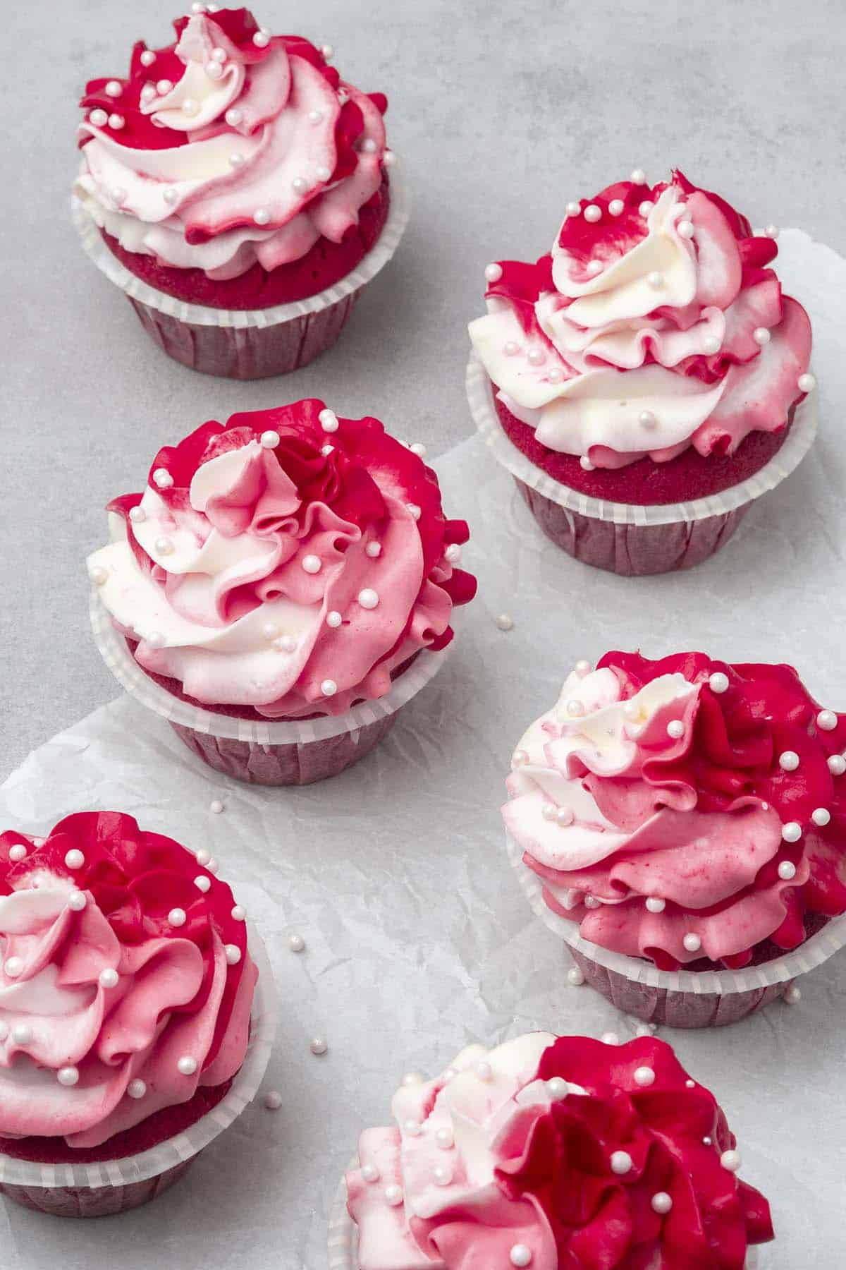 6 Pink cupcakes decorated with marbled colored frosting on a white surface.
