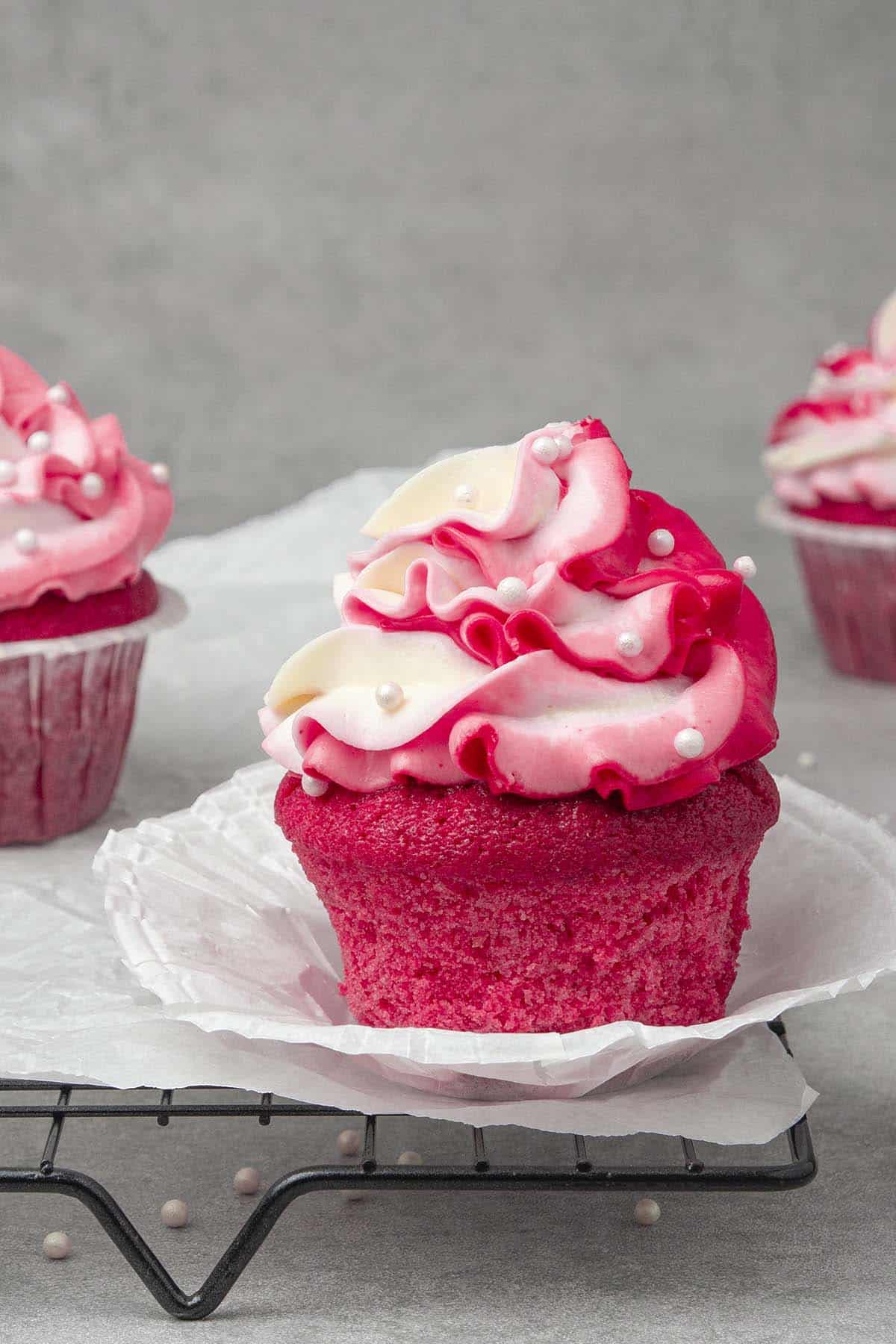 3 Pink cupcakes on a cooling rack.