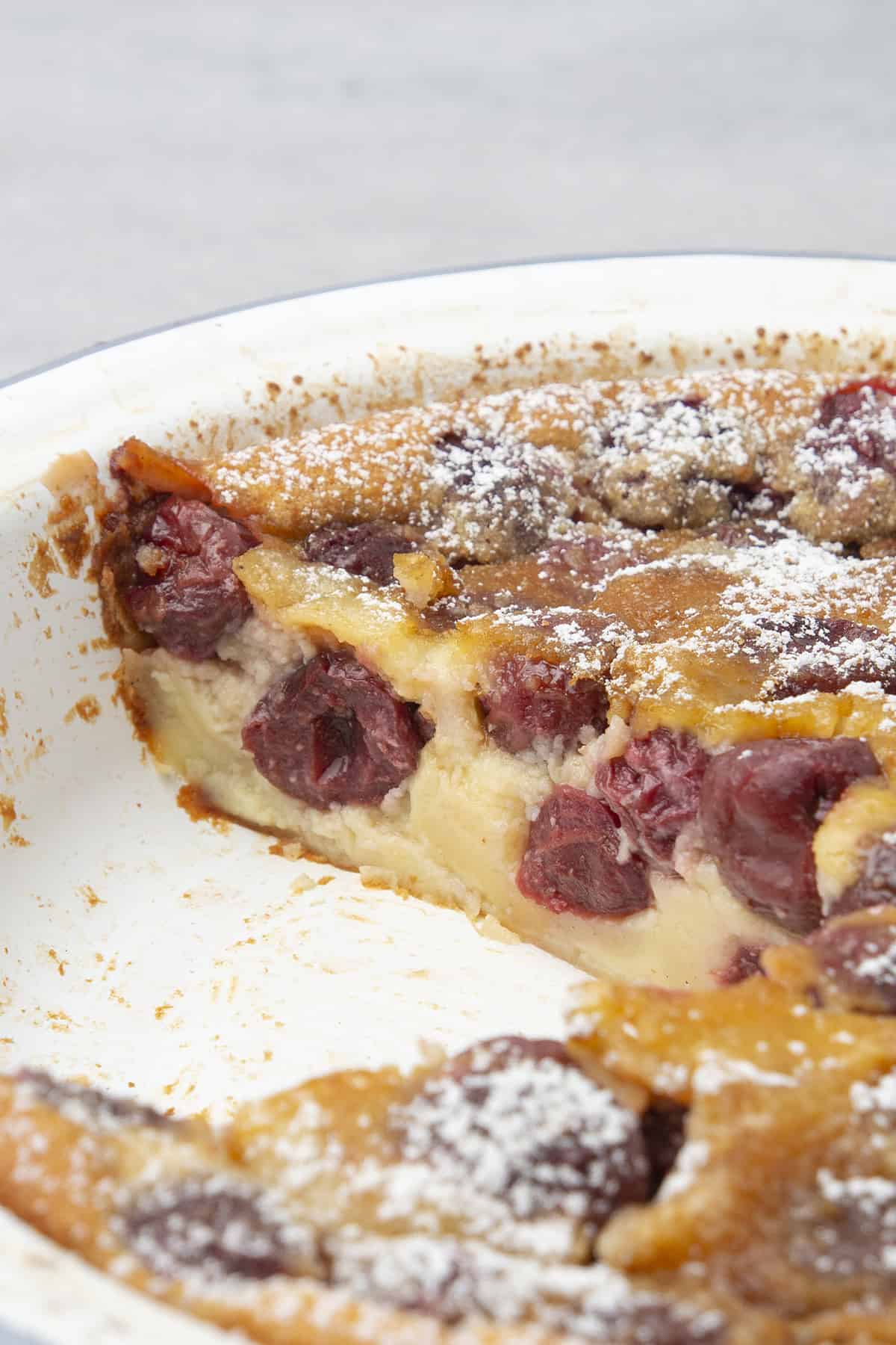 Clafoutis in a white pie tin  and a slice of it cut off.