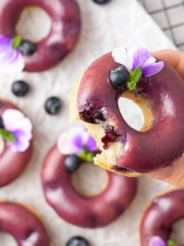 Blueberry baked donuts on a cooling rack and a hand holding one of the donut.