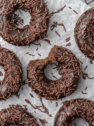 6 baked chocolate donuts on a cooling rack.