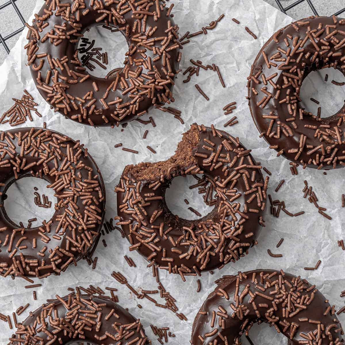 6 baked chocolate donuts on a cooling rack.