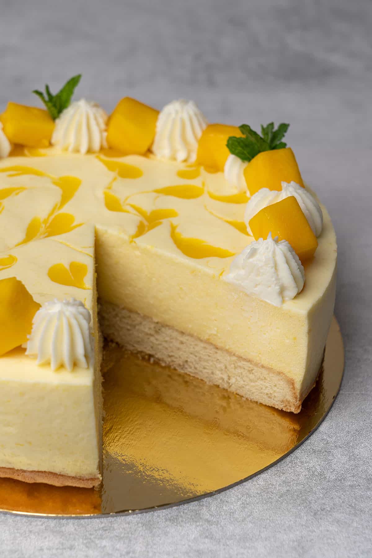 mango mousse cake with a slice taken out of it against a grey background