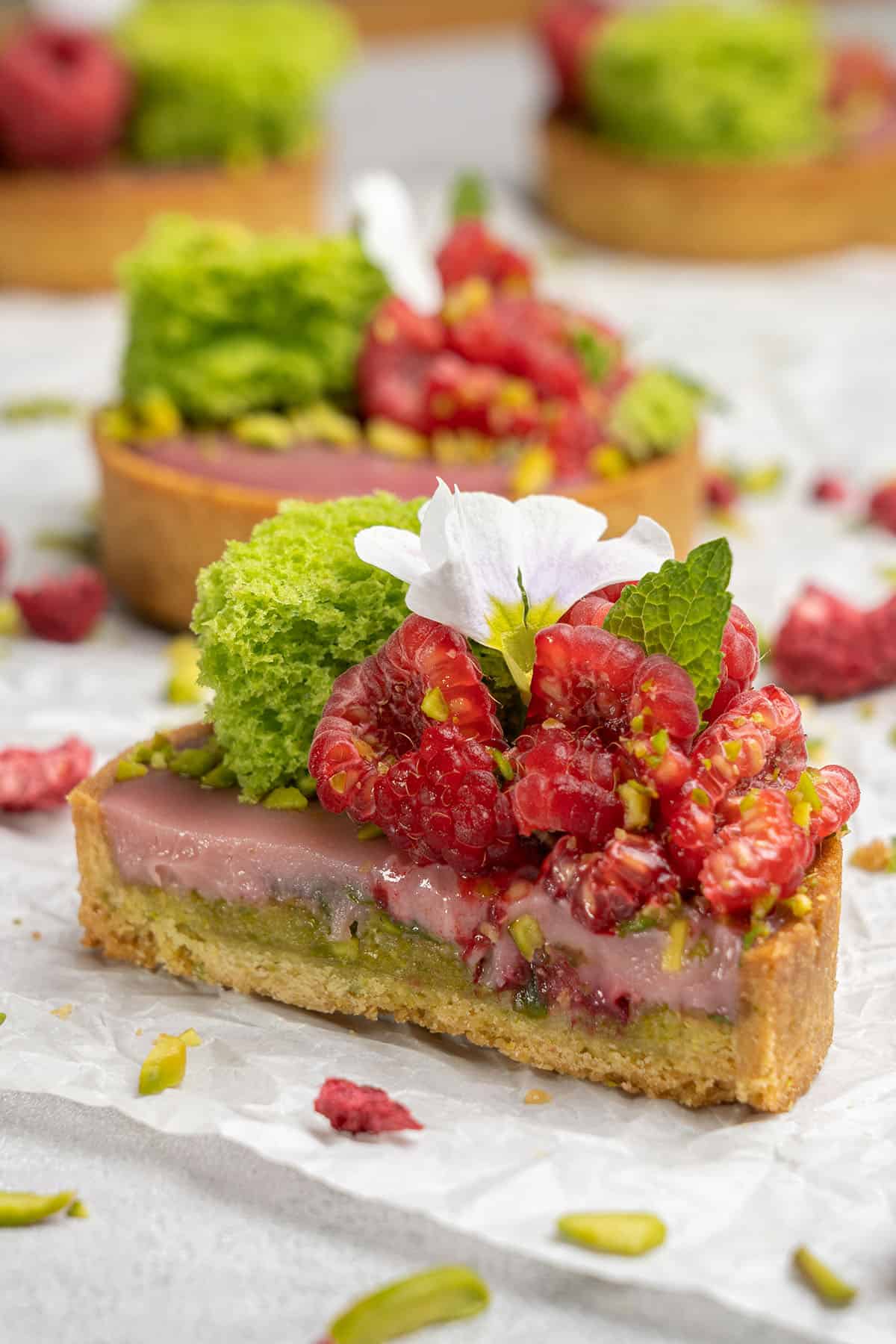 Pistachio raspberry tarts cut half on a white paper.