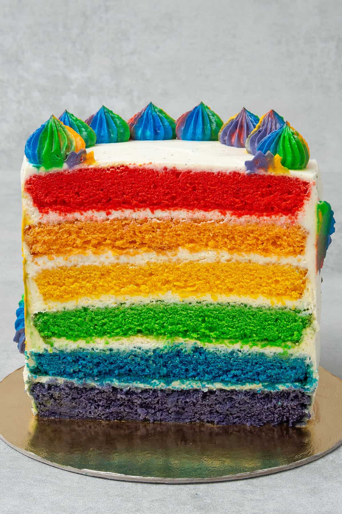 A half Rainbow cake on a golden paper plate.