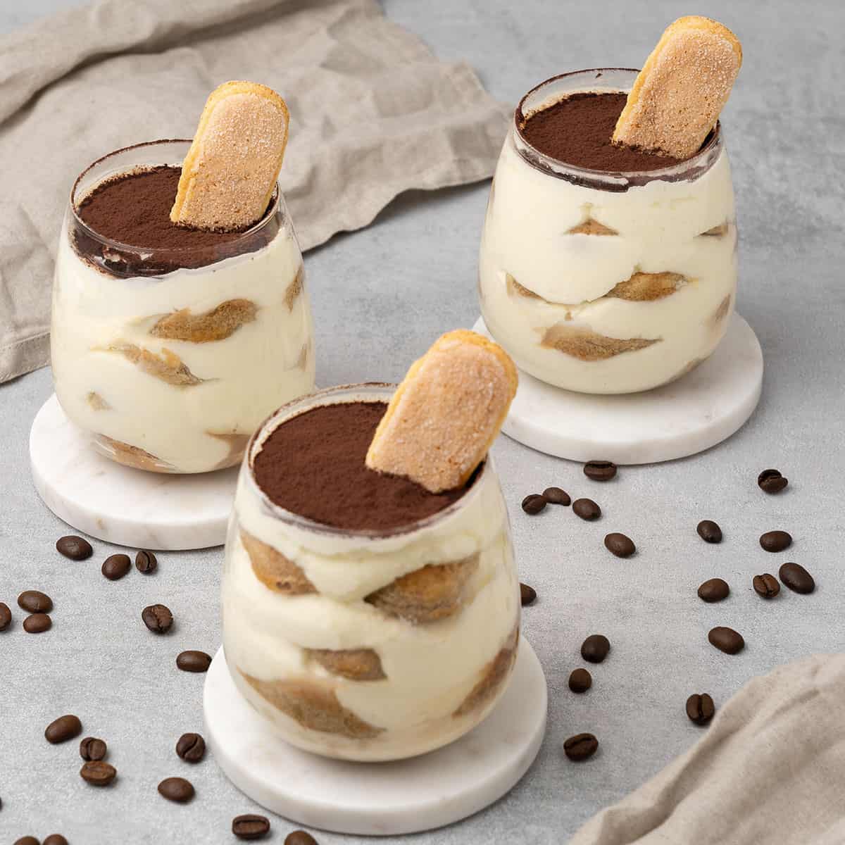 3 Mini tiramisu cups in a glass on a table top.