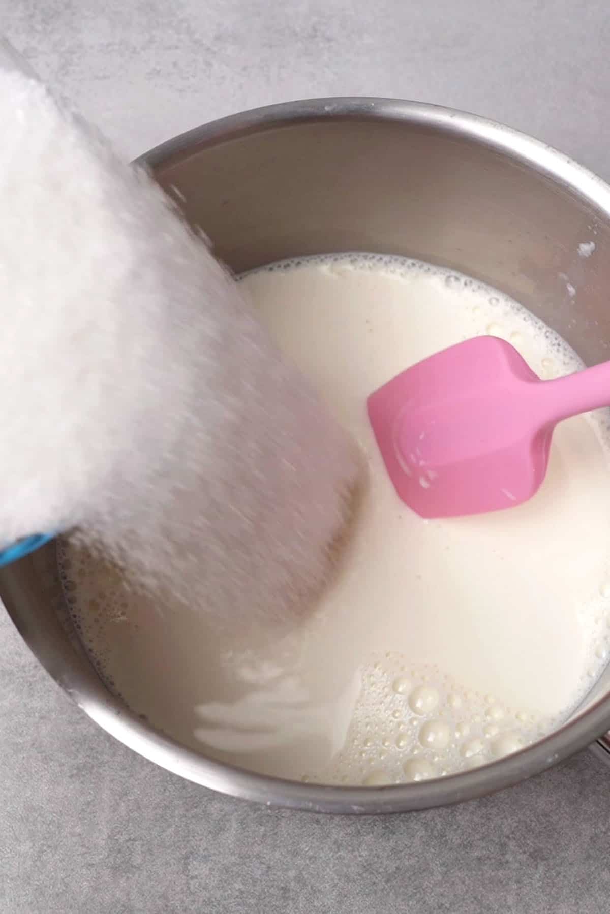 Adding sugar to milk in a put to create condensed milk.