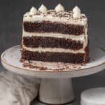 A half Chocolate cake with cream cheese frosting on a cake stand.