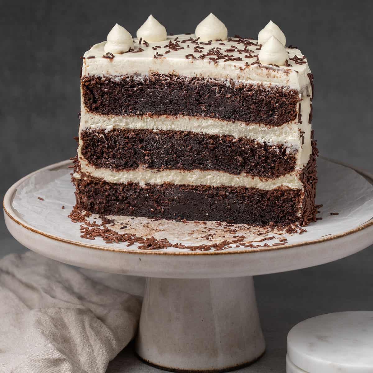 A half Chocolate cake with cream cheese frosting on a cake stand.