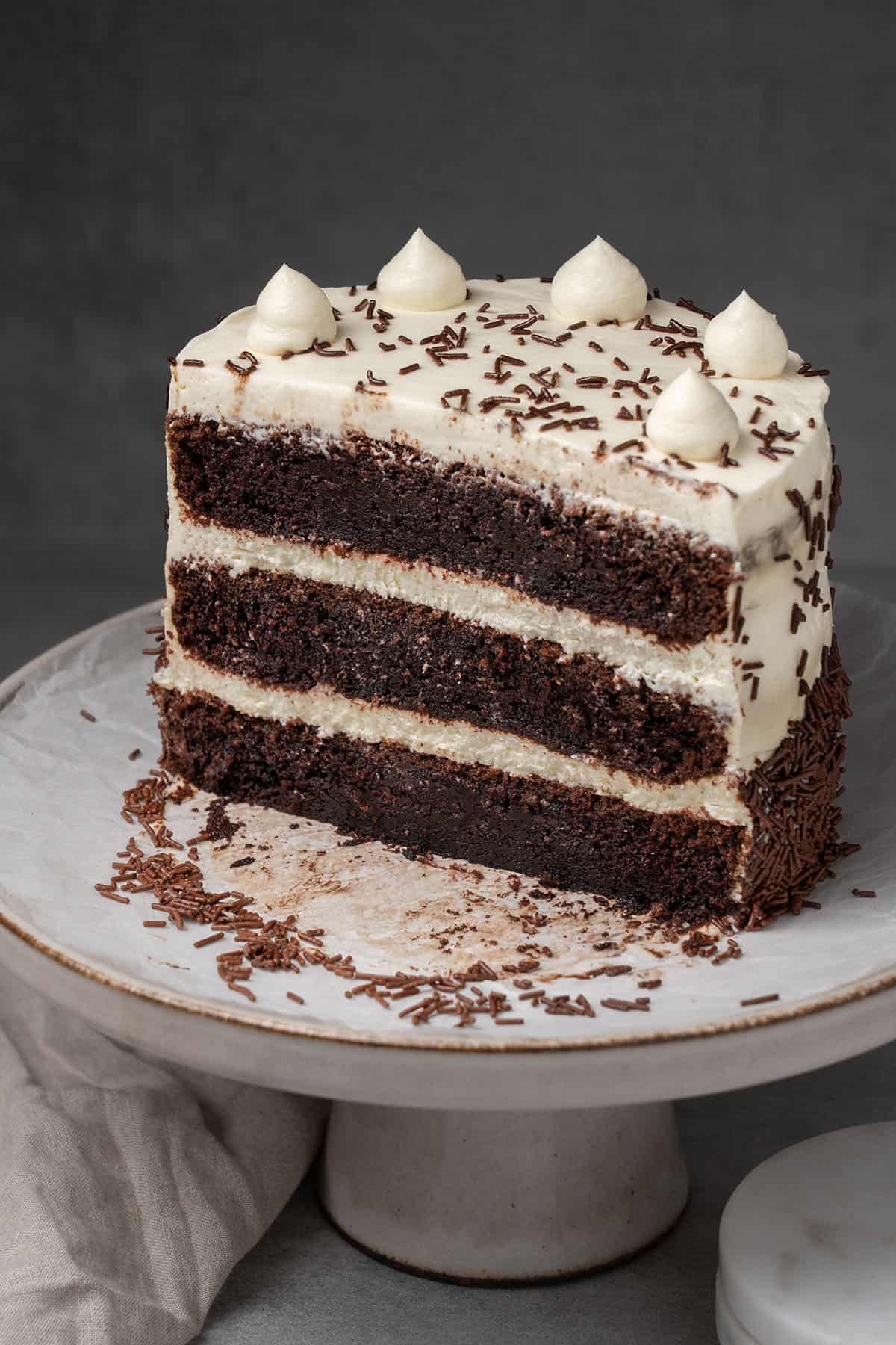 A half Chocolate cake with cream cheese frosting on a cake stand.