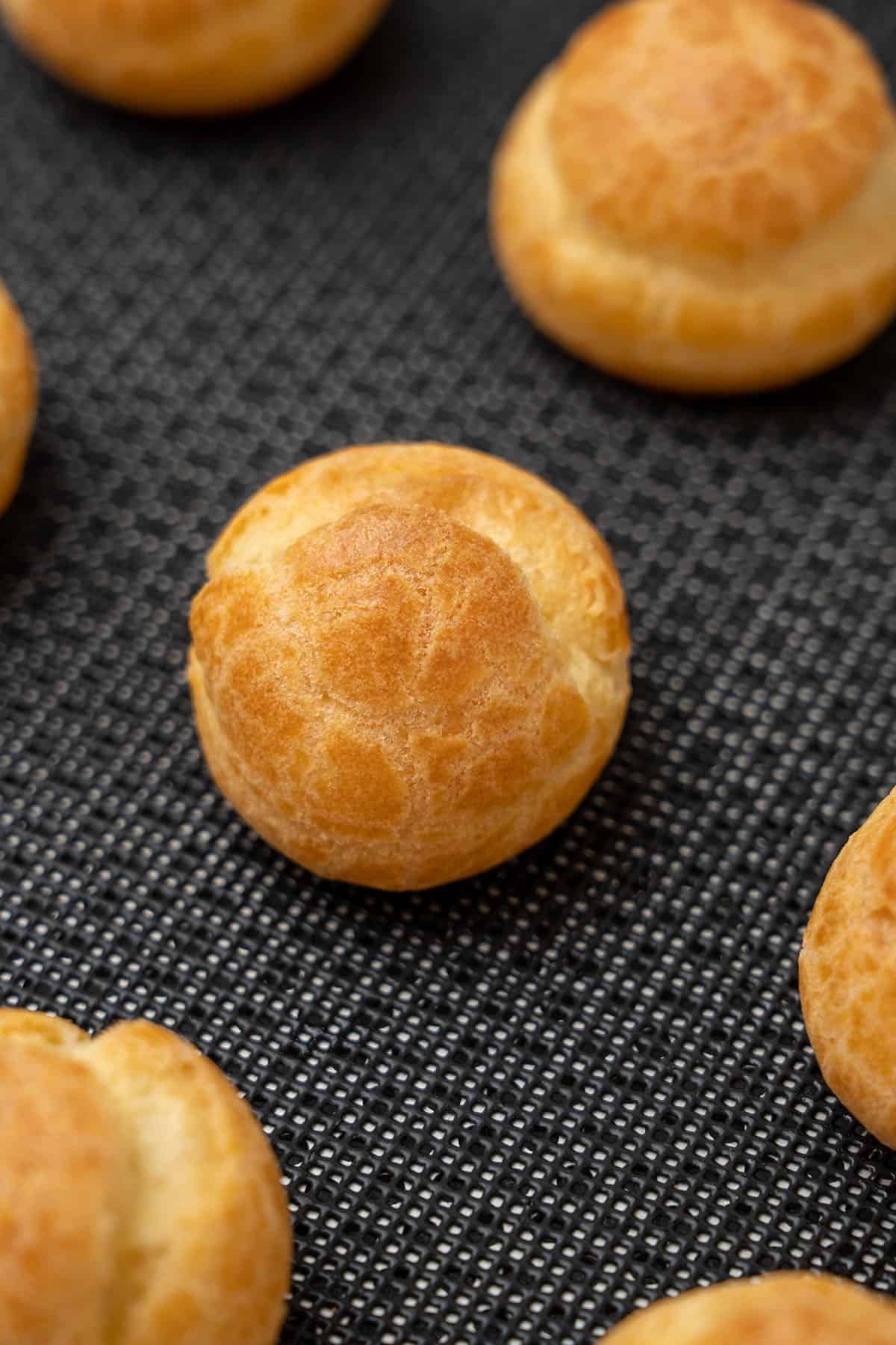 Choux pastry cream puffs on a baking mat.