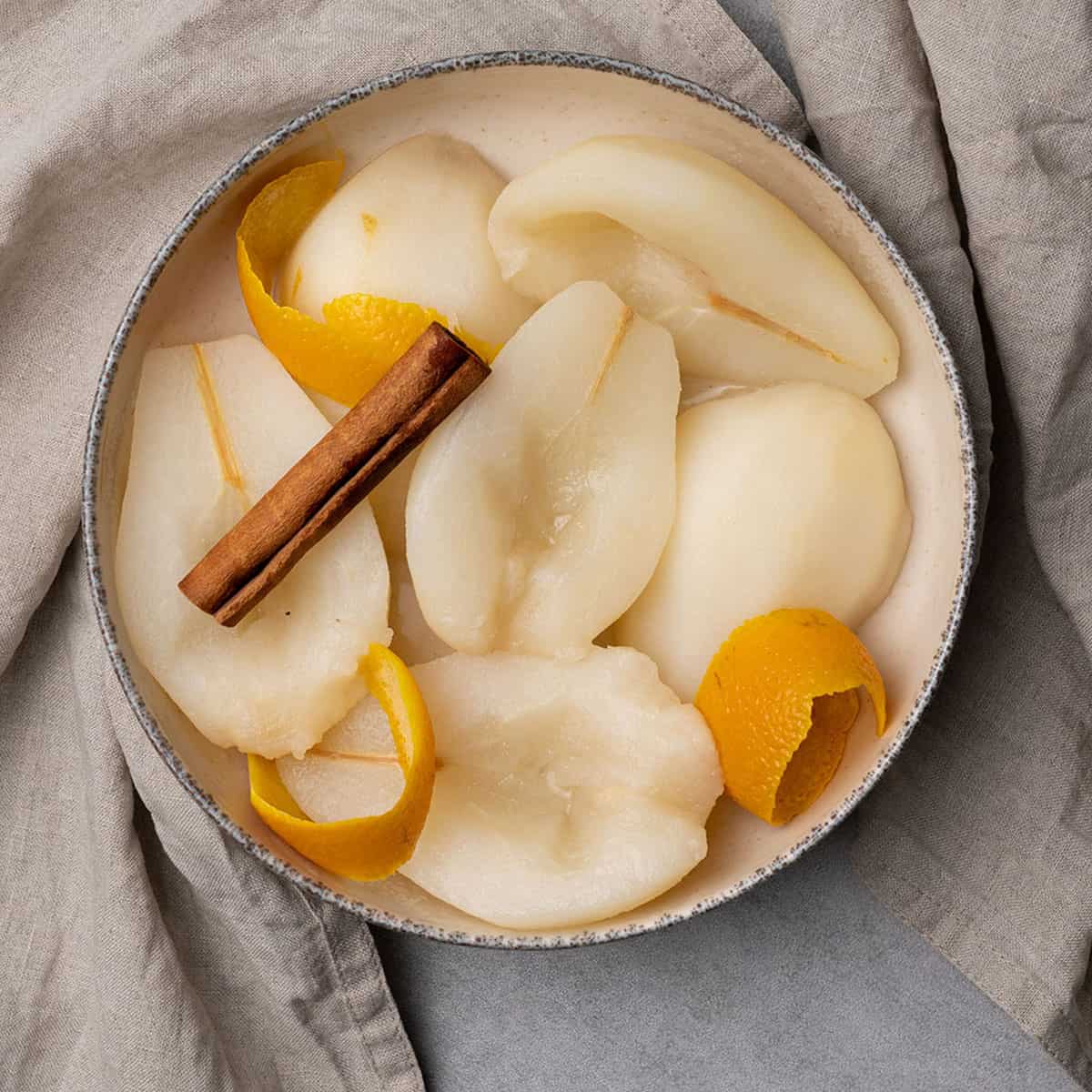 Poached pear in a bowl with cinnamon and orange peel.