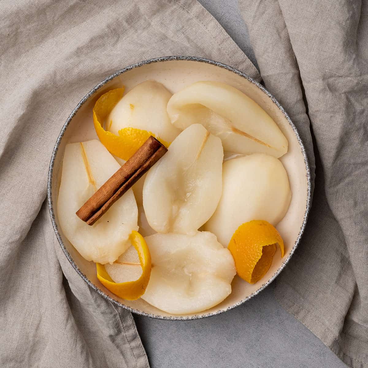 Poached pear in a bowl with cinnamon and orange peel.