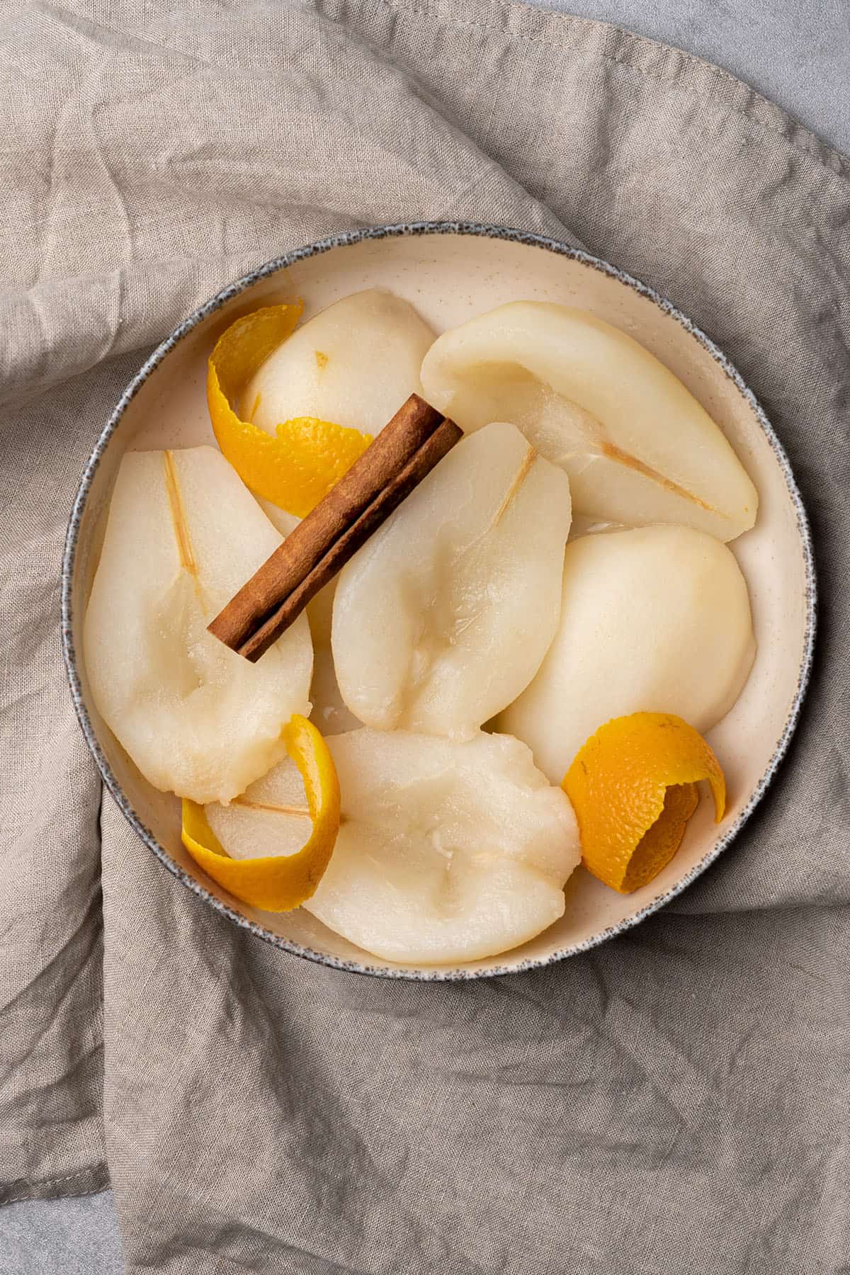 Poached pear in a bowl with cinnamon and orange peel.