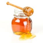 a jar full of honey with a dripper on top.