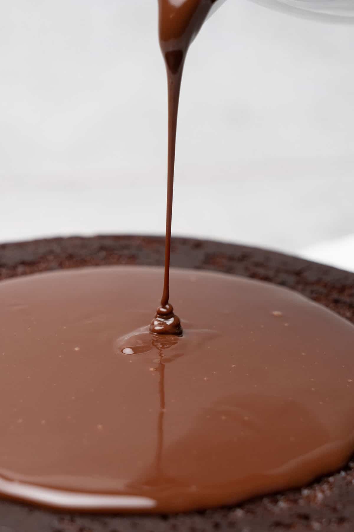 pouring chocolate ganache topping on a chocolate sponge cake.