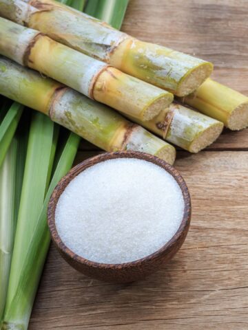 sugar cane sticks and granulated sugar in a cup.