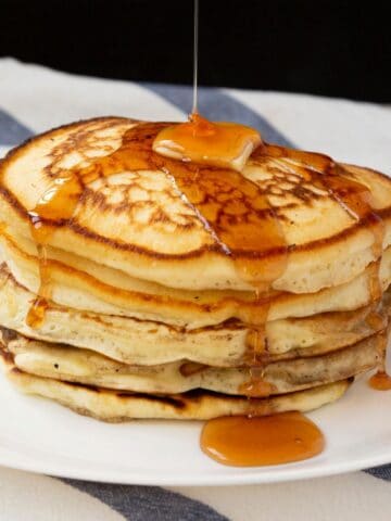 pouring maple syrup on a stack of pancakes.