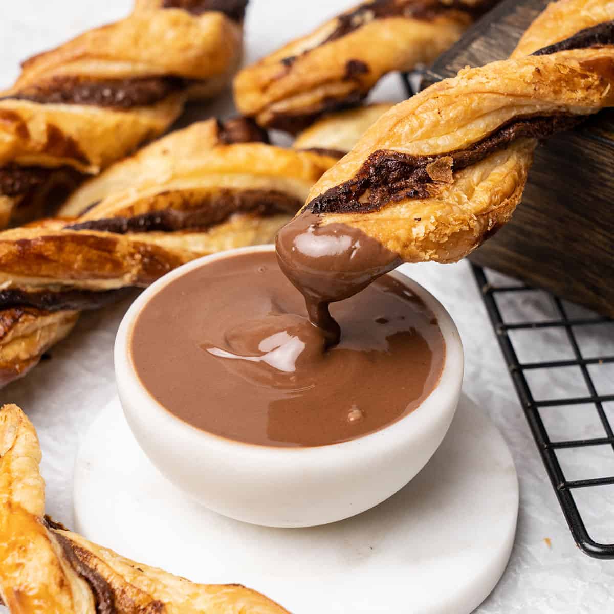 Nutella puff pastry twists dipping in chocolate cream.