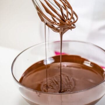 dipping a whisk into a bowl of melted chocolate.