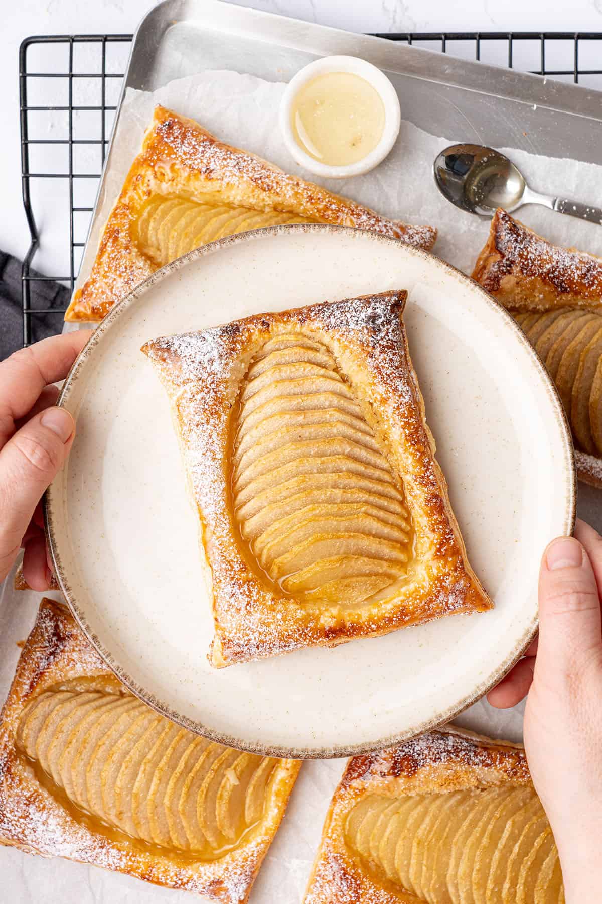 a hand holding a plate with pear puff pastry tart.