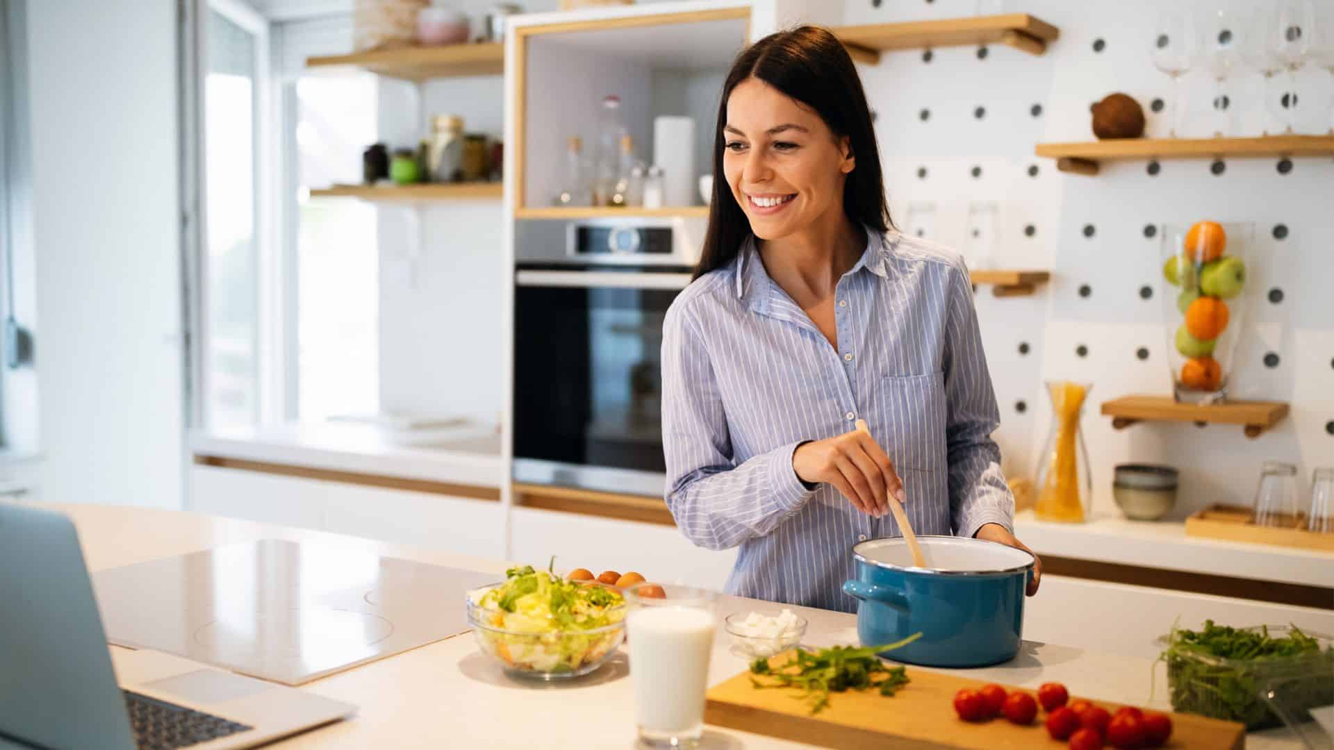 Happy woman learning how to cook from her laptop.