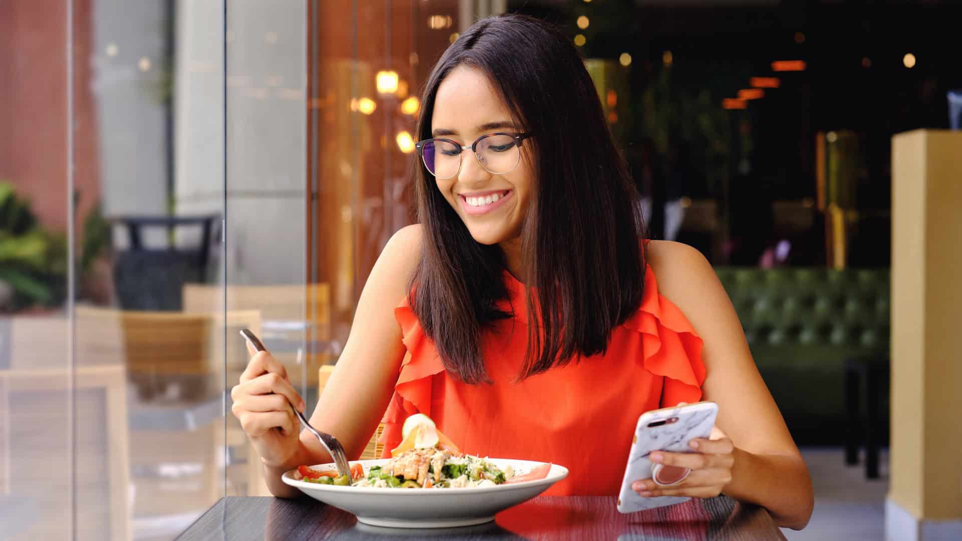 happy woman eating alone in a restaurant with her phone