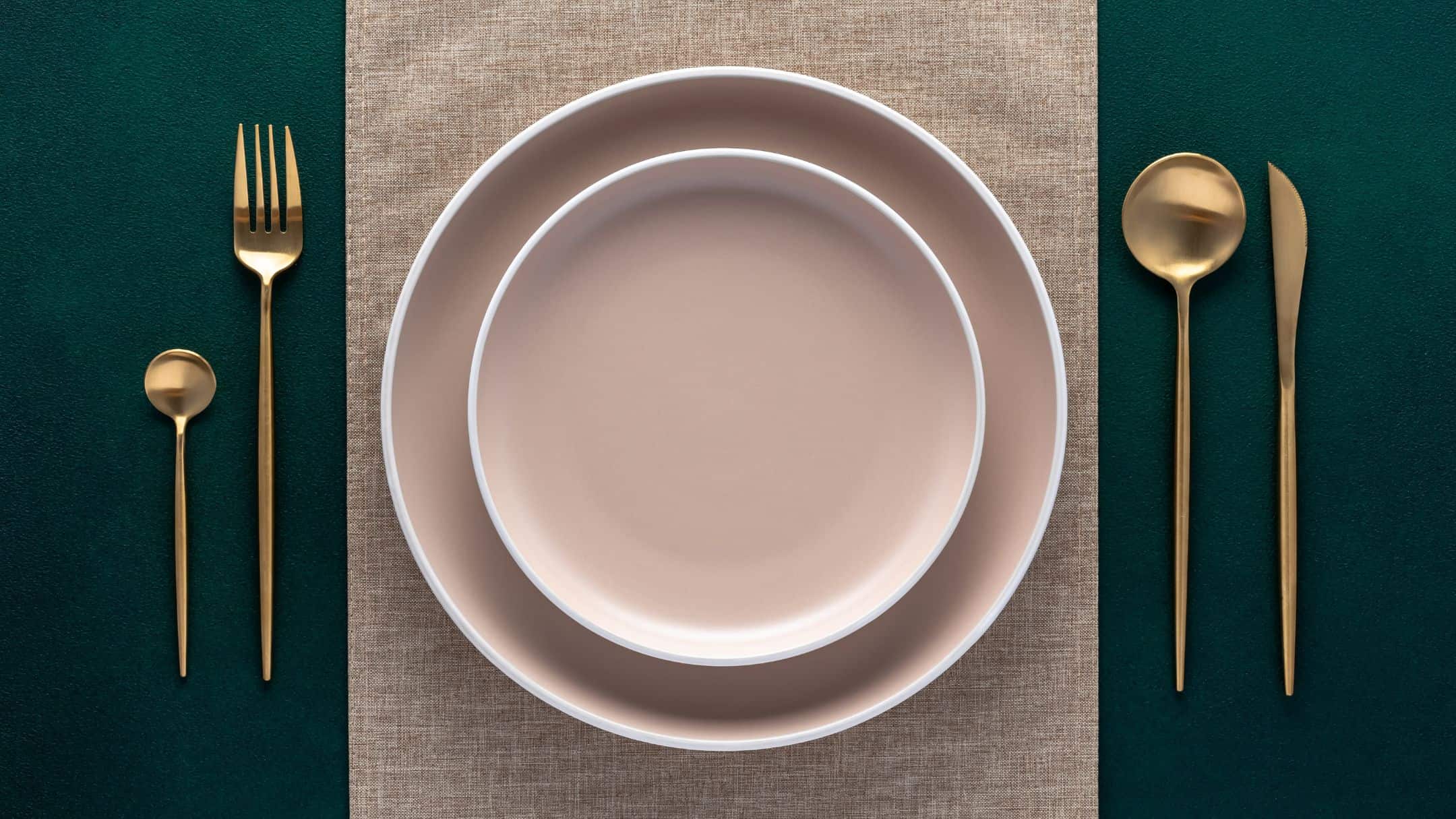 Empty plates and gold cutlery on dark green background