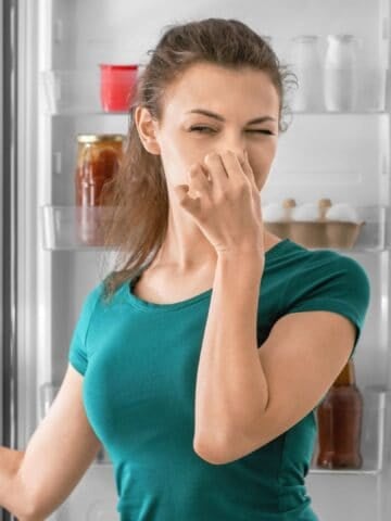Young Woman Feeling Bad Smell from Refrigerator in Kitchen