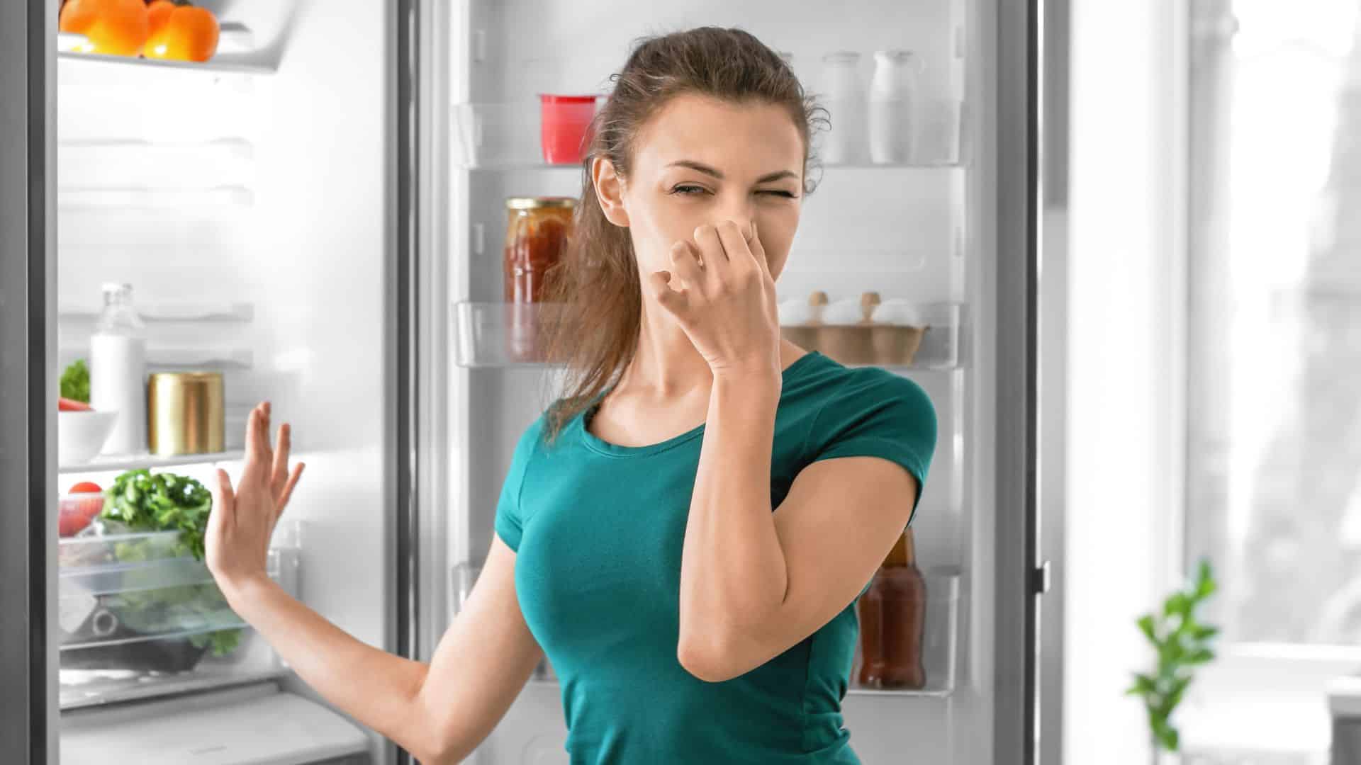 Young Woman Feeling Bad Smell from Refrigerator in Kitchen