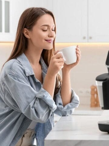 Young woman enjoying fresh aromatic coffee near machine in kitchen