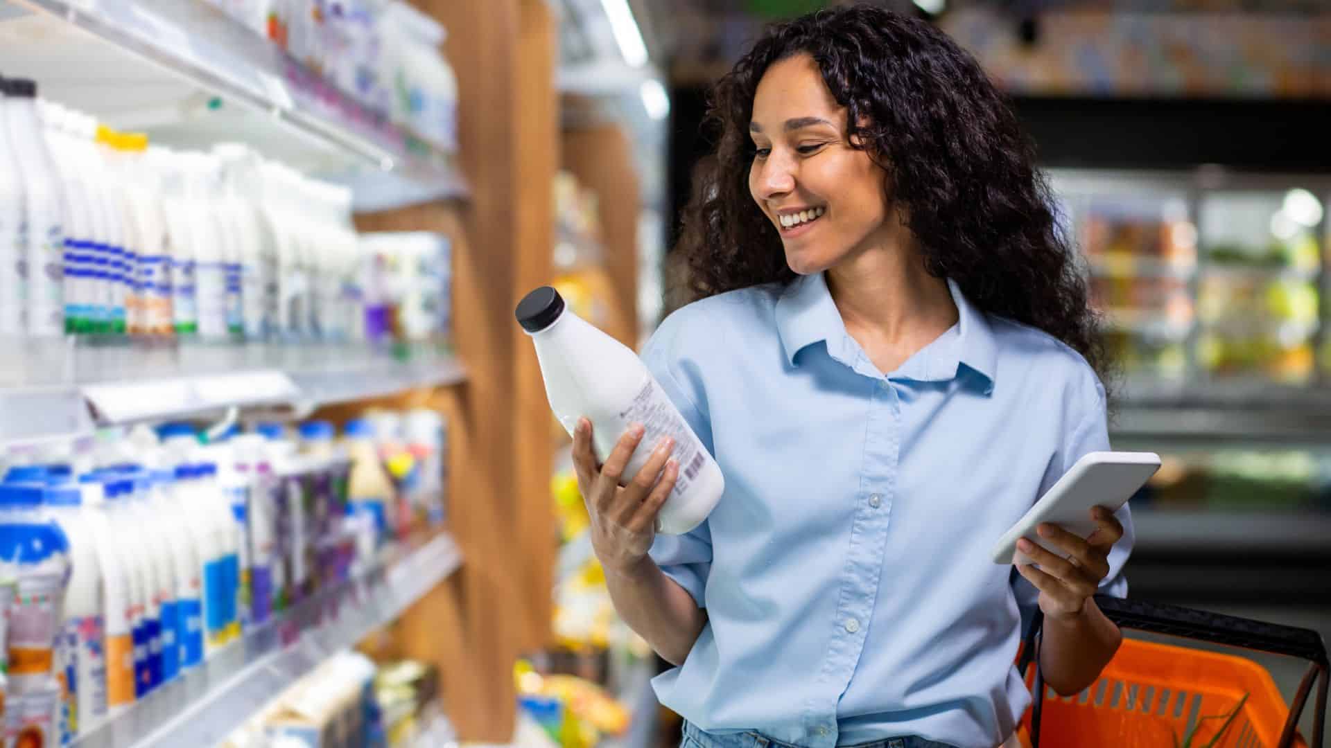 Joyful young woman with curly hair selects products in supermarket.