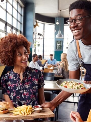 Waiter Serving Group Of Female Friends Meeting For Drinks And Food In Restaurant