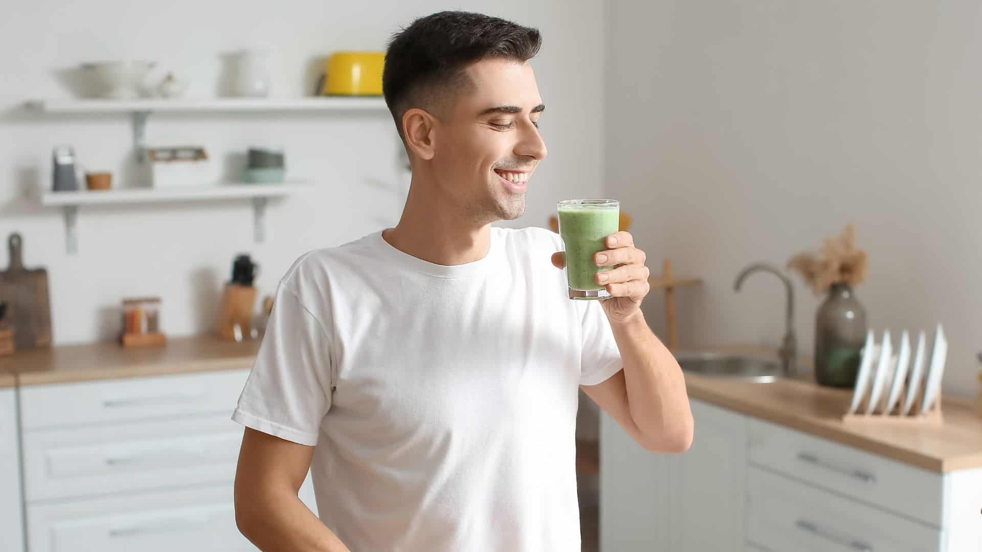Young man drinking healthy green smoothie in kitchen