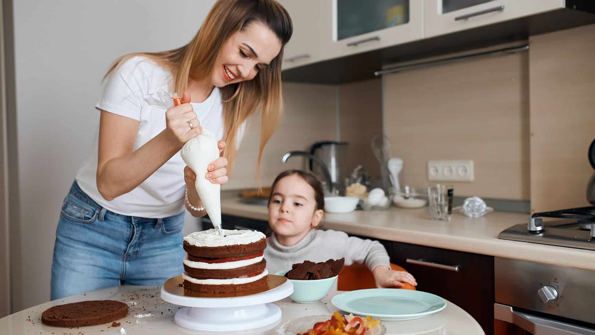 woman and her kid frosting a cake with whipped cream