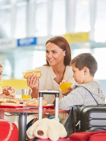 Delicious family enjoying pizza at airport cafe with luggage around.