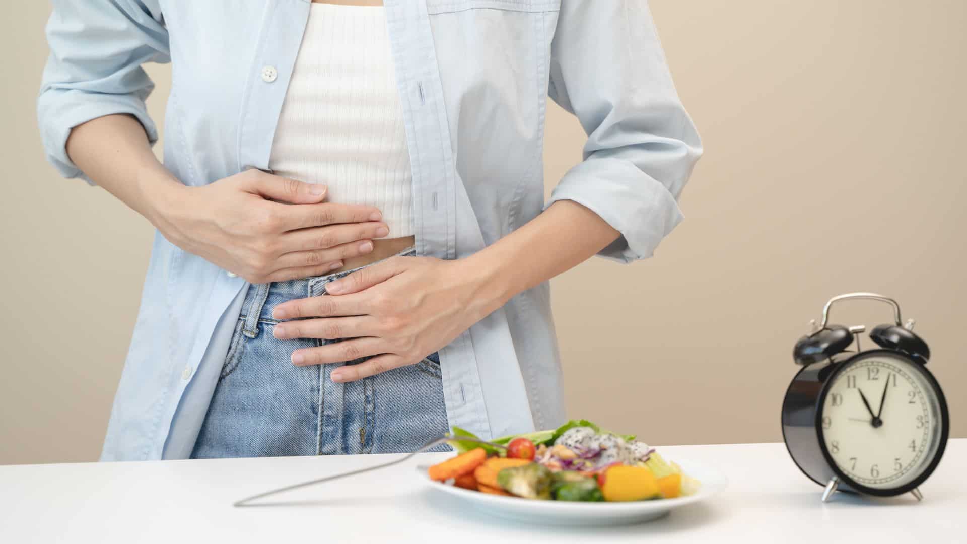 hands on stomach with food on table