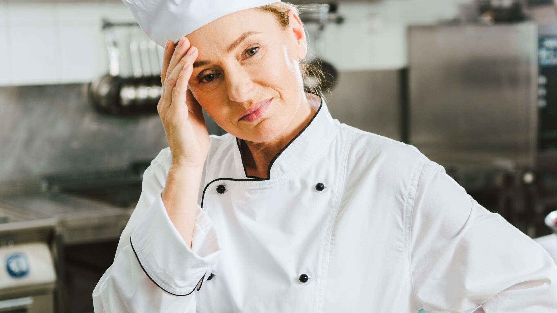 tired female chef in uniform having headache in restaurant kitchen