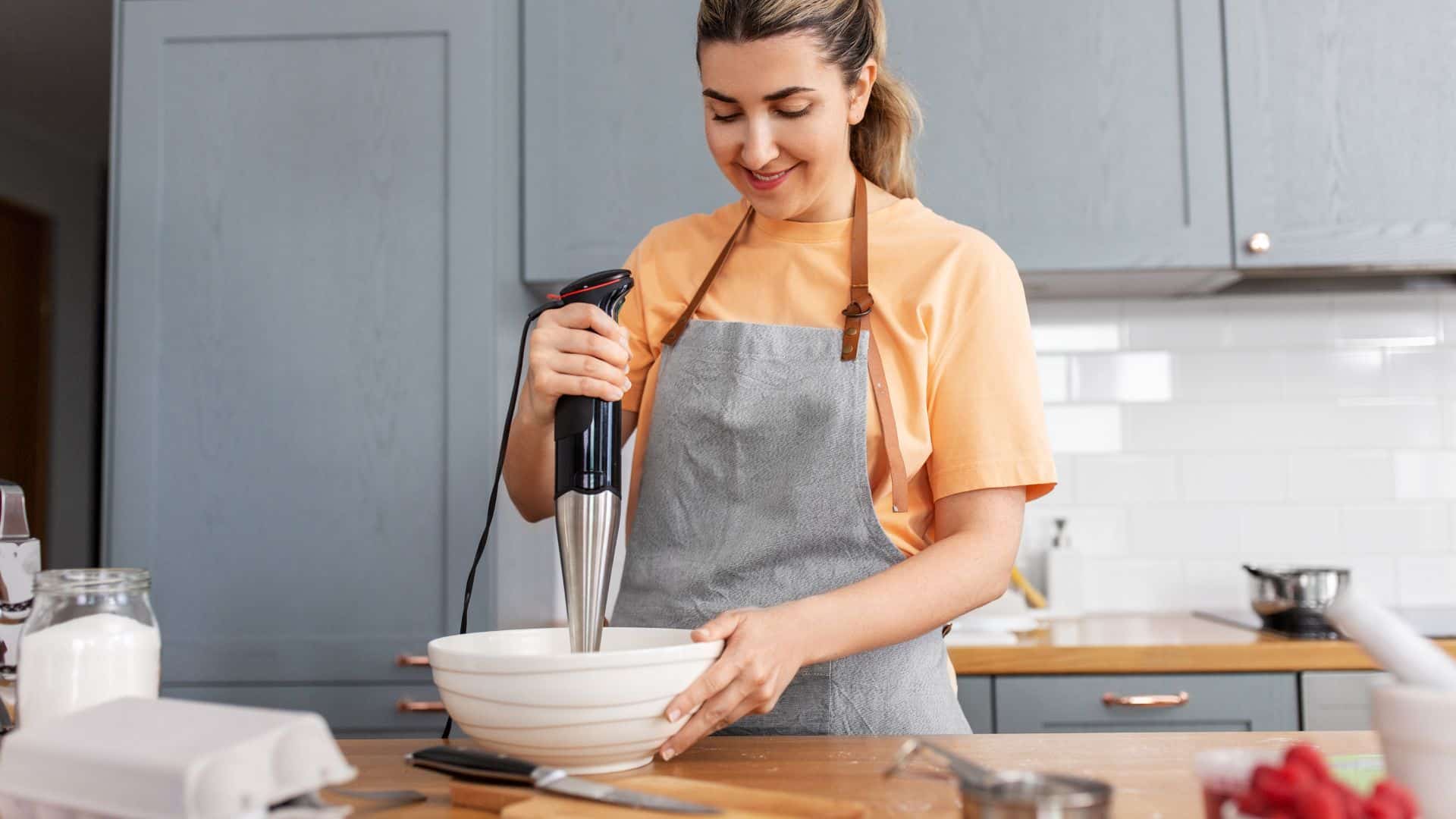 woman cooking food on kitchen at home and using immersion blender